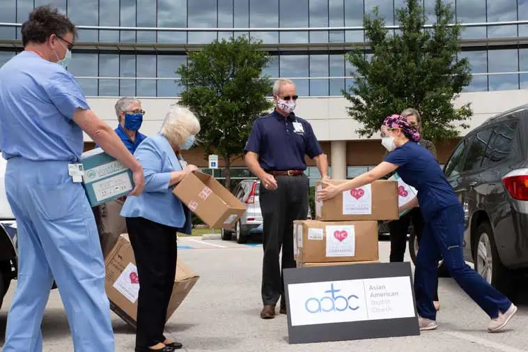 People wearing masks distributing boxes of supplies outside a modern building.