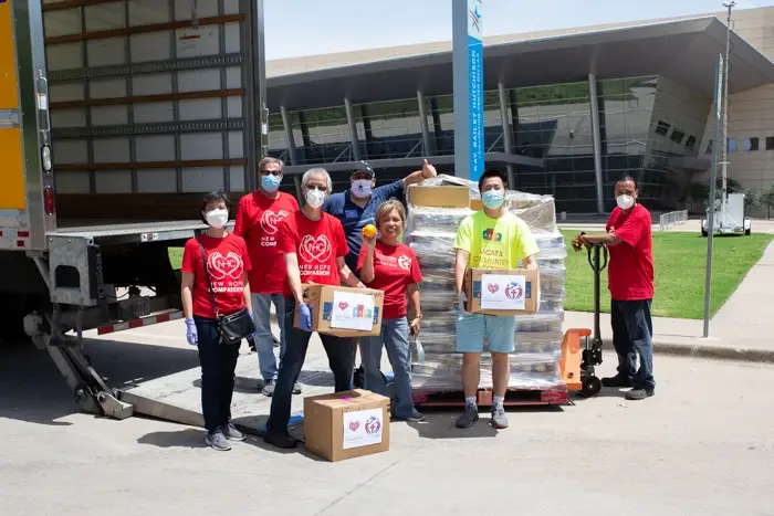 Group of volunteers with masks holding donation boxes outside a building.