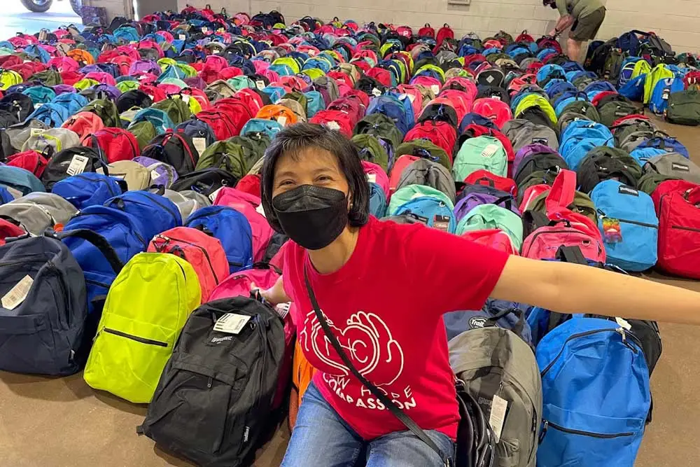 Person in red shirt and black mask among many colourful backpacks.