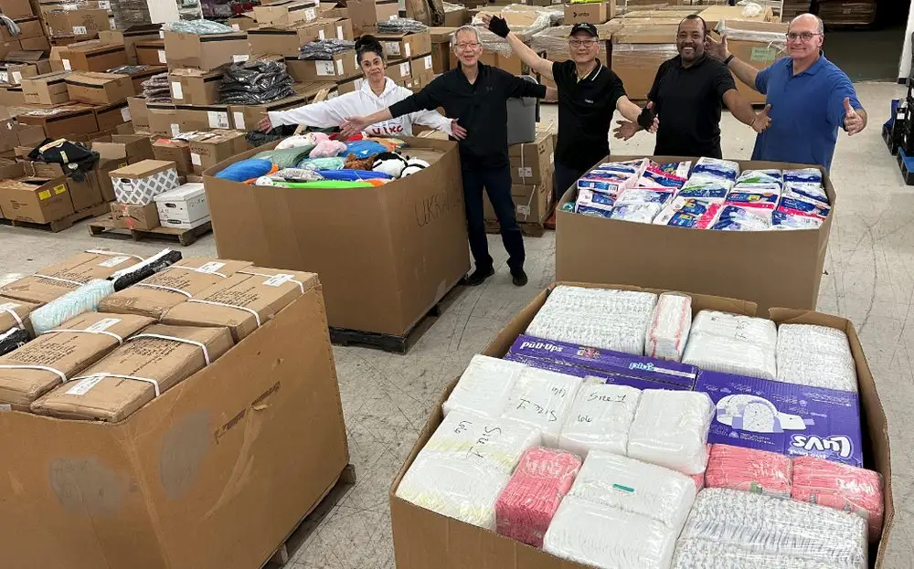 Three people standing by large boxes filled with donated items in a warehouse.